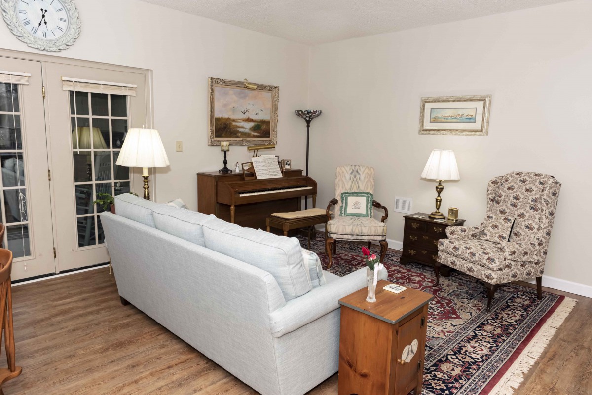 A cozy living room featuring a sofa, piano, and armchairs with warm lighting.