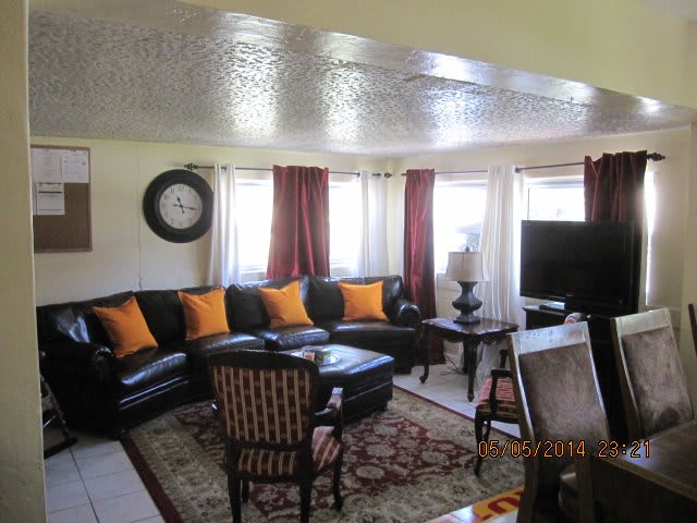 A cozy living room with a black leather sofa, orange pillows, a television, and an armchair.