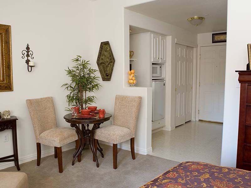 A cozy living space featuring a small dining area with two chairs, a round wooden table, and decorative elements including a plant and wall art.