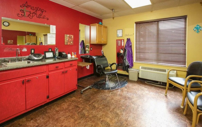 A cozy hair salon with vibrant red and yellow walls, featuring a styling chair, mirrors, and hairdressing equipment.