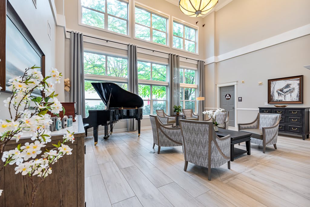 A spacious living room with a grand piano, featuring high ceilings and large windows letting in natural light.