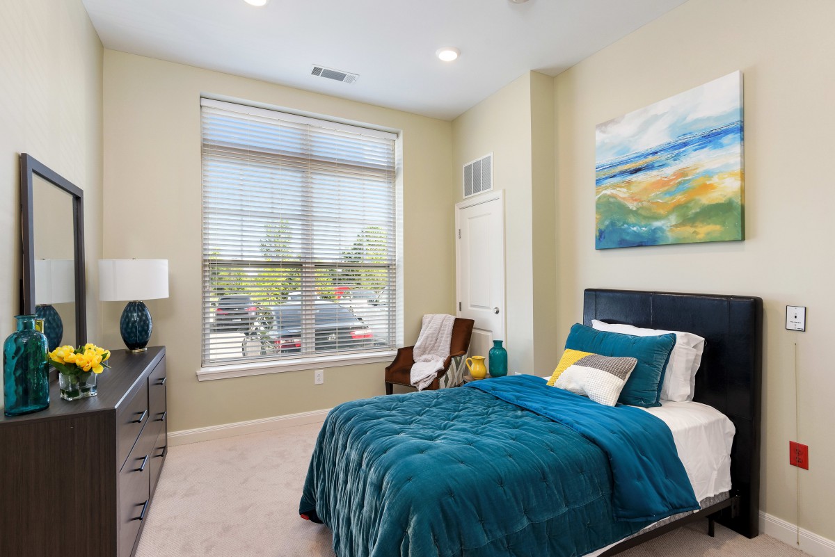 A modern bedroom with teal bedding, large window, and contemporary decor.