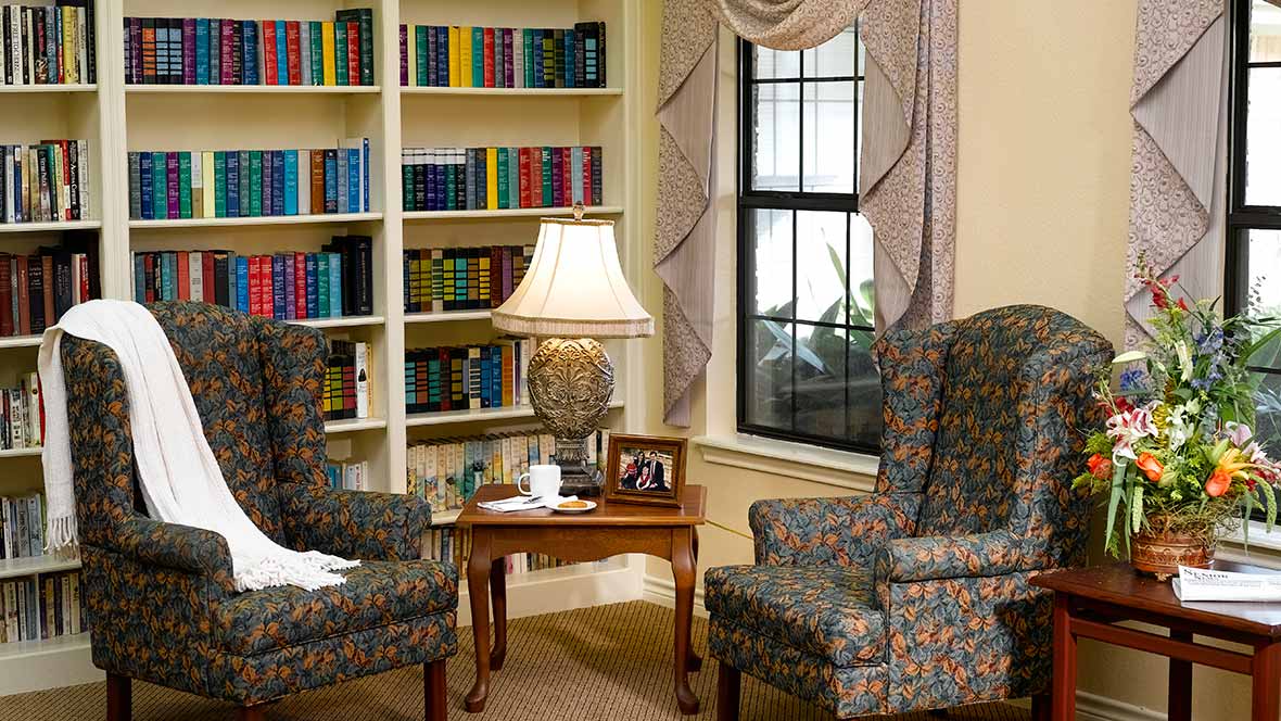 A cozy living room featuring a bookshelf, two patterned armchairs, and a coffee table with a lamp.
