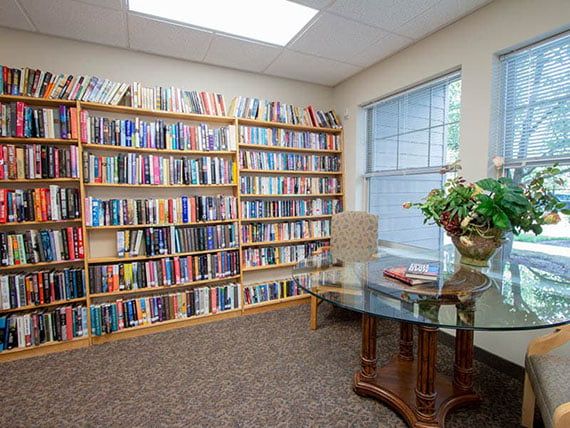 A cozy office space with a large bookshelf filled with books and a glass table.