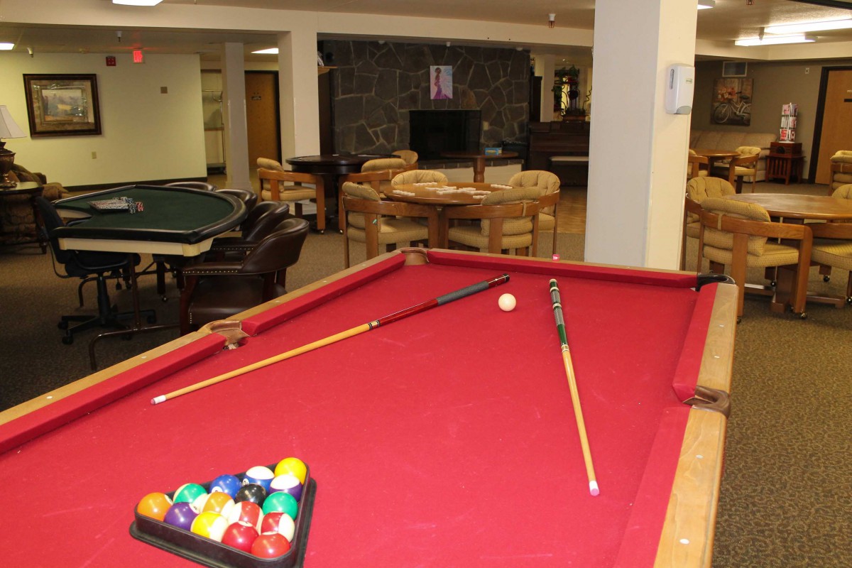A recreational game room featuring a red pool table with cue sticks and balls arranged for play.