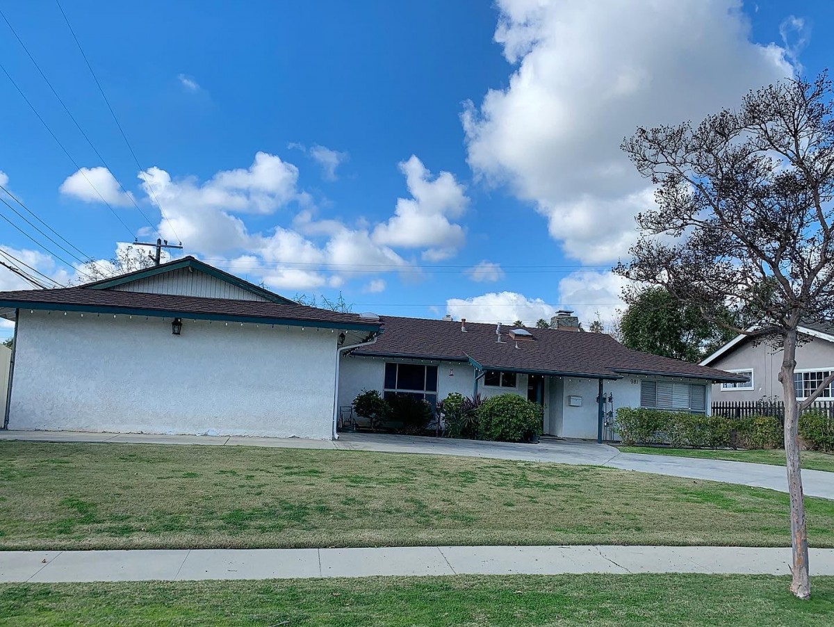 A suburban house with a front lawn and a driveway under a partly cloudy sky.