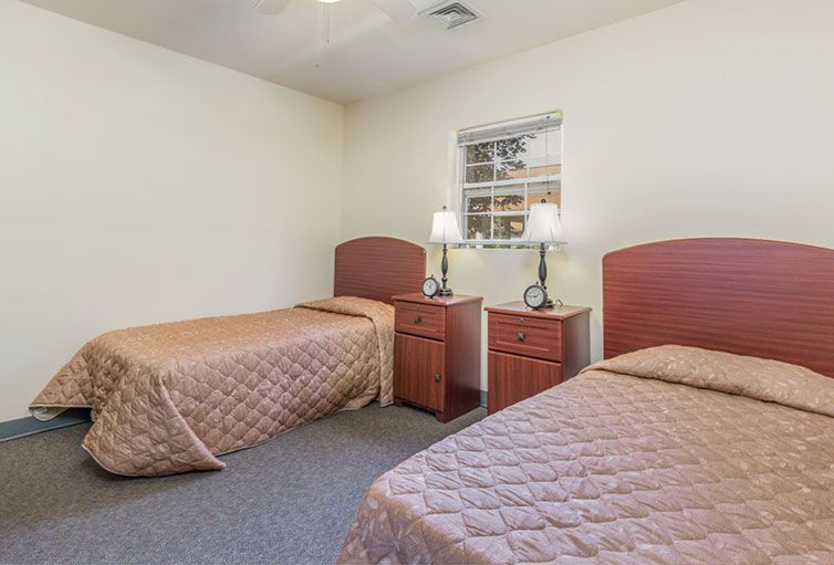 A simple bedroom featuring two twin beds with matching quilts, wooden headboards, and bedside tables with lamps.