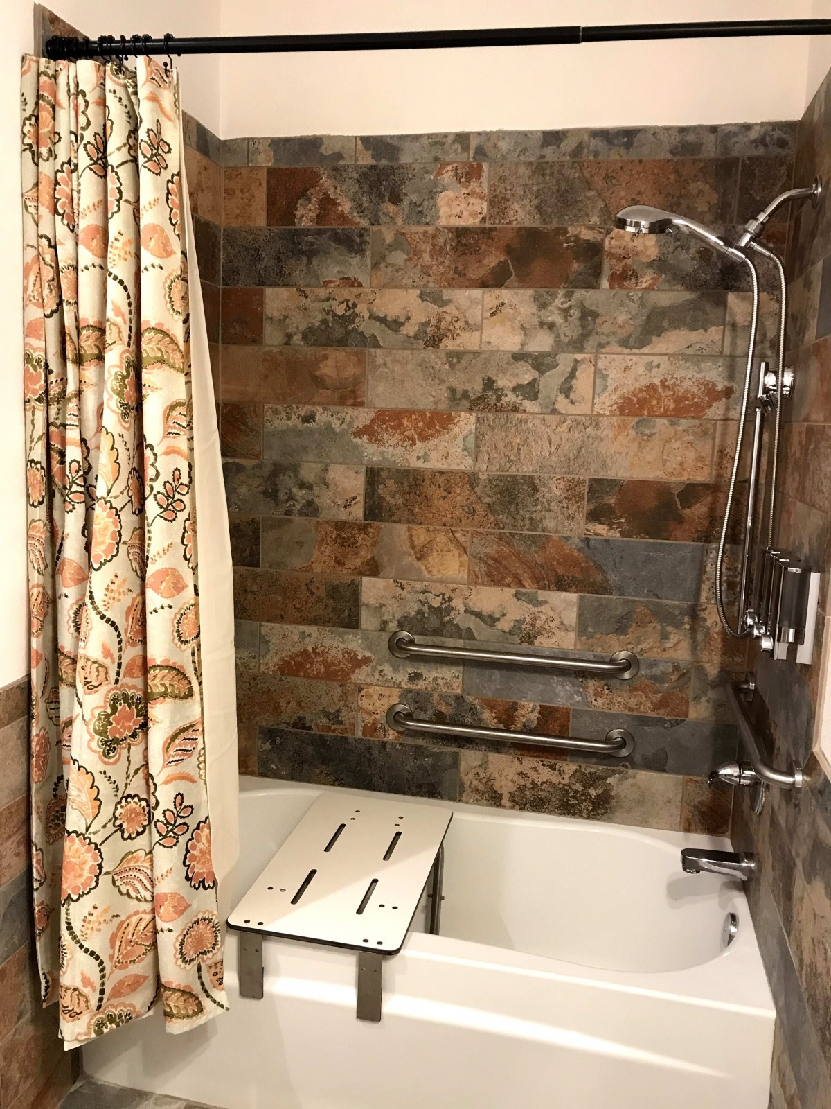 A bathroom featuring a bathtub with tiled walls, a decorative shower curtain, and a shower head.