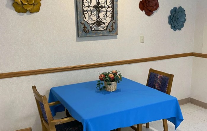A dining area with a blue tablecloth, decorated with a floral centerpiece and wall art.