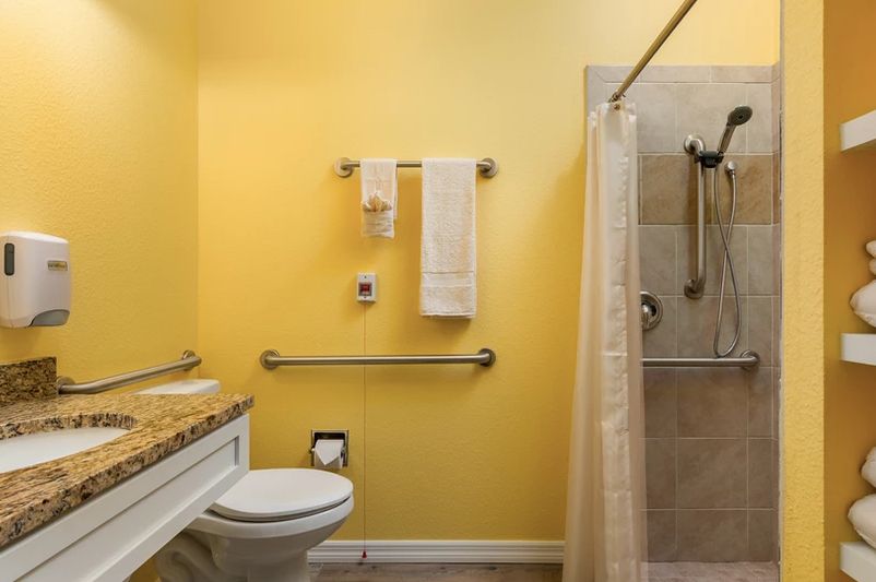 A bathroom with yellow walls featuring a shower, toilet, and accessibility features like grab bars and towel racks.