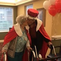 An elderly couple dressed as a king and queen share a sweet moment during a celebration.