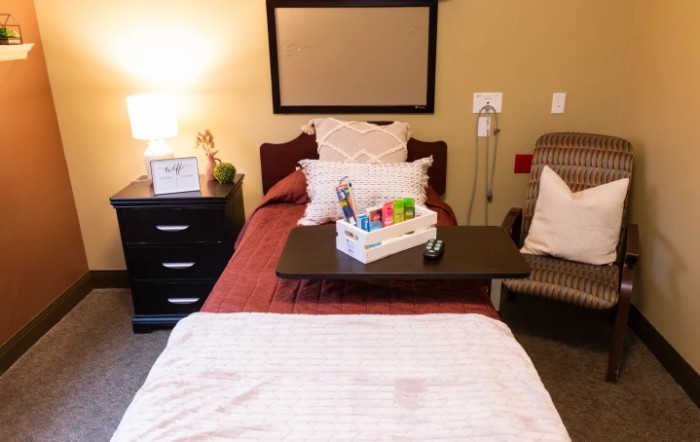 A hospital room with a well-made bed, nightstand, and medical equipment.