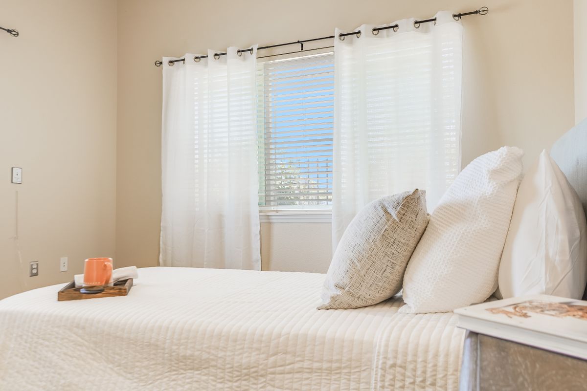 A bright bedroom with a neatly made bed and sheer curtains allowing natural light to fill the room.