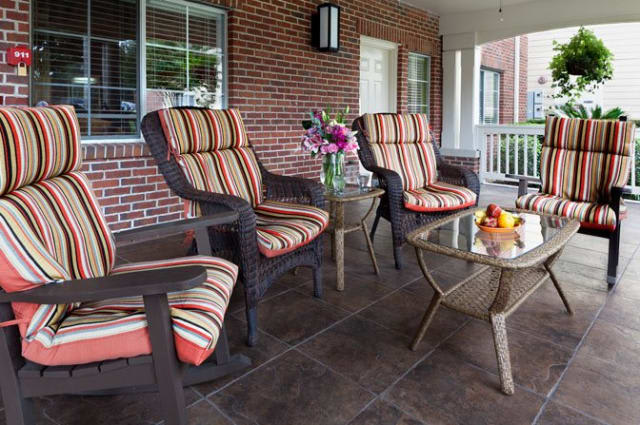 A cozy porch setup with striped cushioned chairs, a glass table adorned with flowers and fruit.