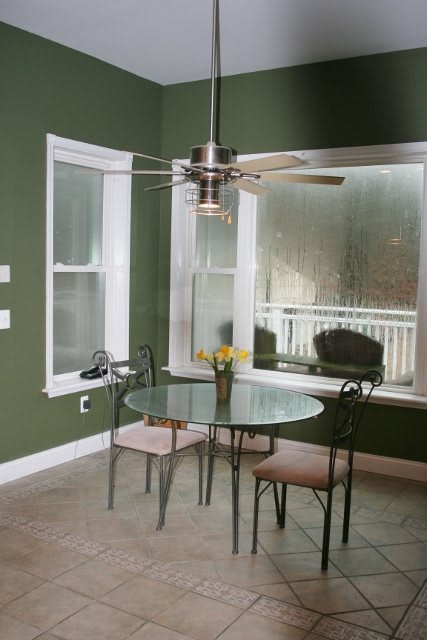 A cozy dining area with a glass table and chairs, set against green walls and large windows.