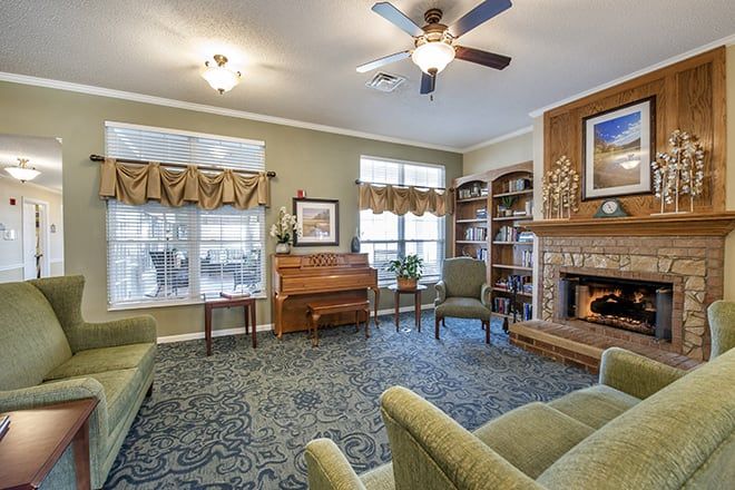 A cozy living room featuring a piano, fireplace, and bookshelves with comfortable seating.