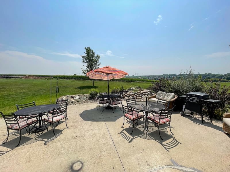An outdoor patio with tables, chairs, and an umbrella overlooking a scenic field on a sunny day.