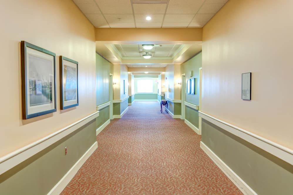 A well-lit hallway with paintings on the walls and a carpeted floor.