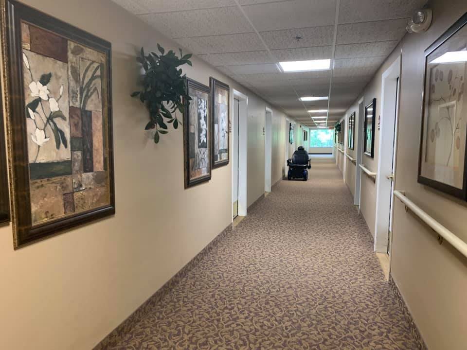 A long hallway in a nursing home with decorated walls and a person in a wheelchair at the end.