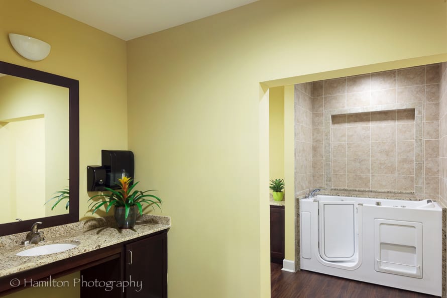 A modern bathroom with a tan color scheme, featuring a bathtub and a washbasin area.