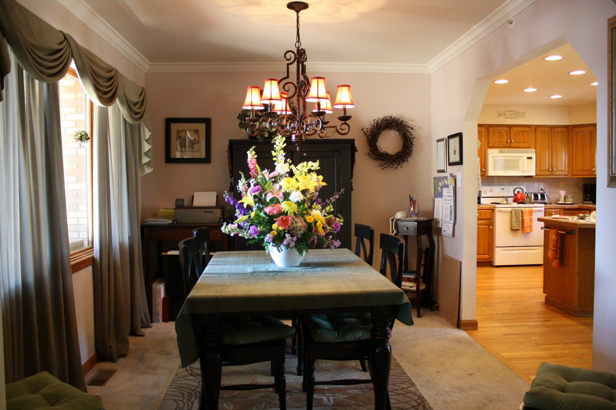 A cozy dining room with a chandelier and a flower arrangement centerpiece.