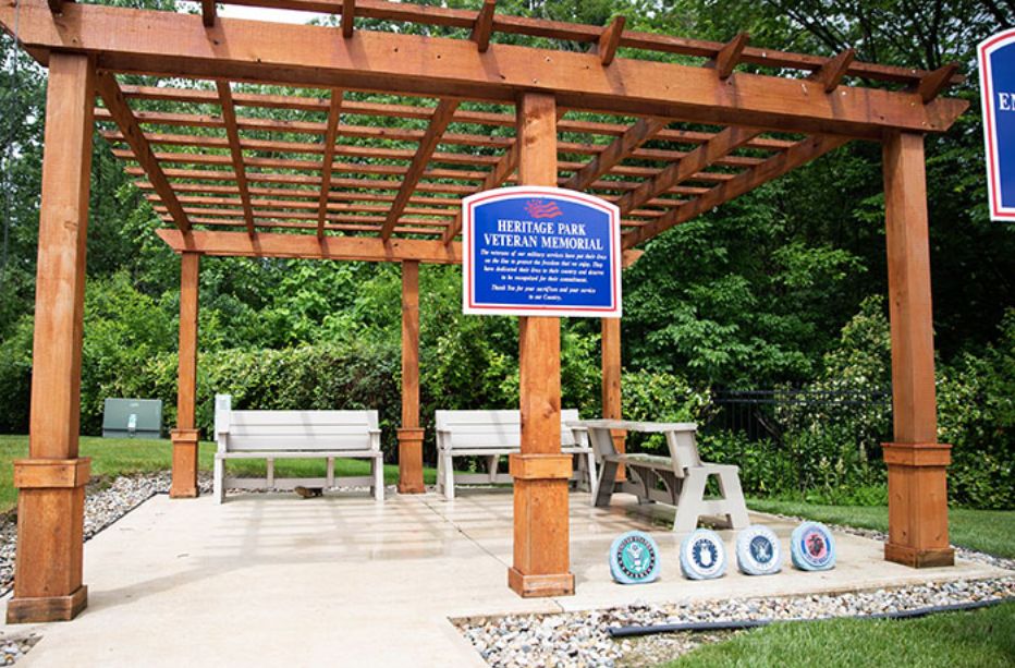 A memorial pergola with benches and military emblems placed in an outdoor garden setting.