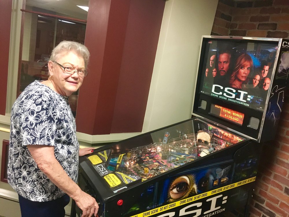 A person enjoying a CSI-themed pinball machine in an arcade setting.