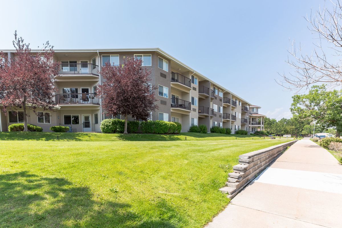 A well-maintained apartment building with lush landscaping and a clear blue sky overhead.