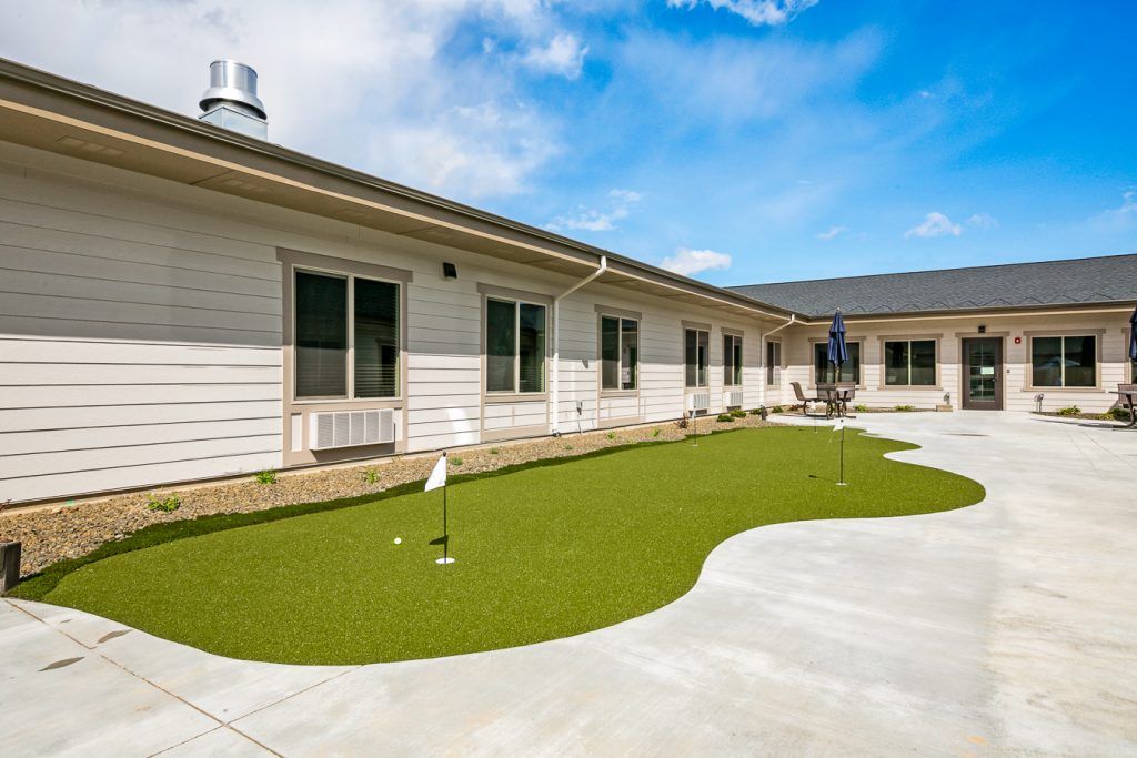 A sunny courtyard featuring a small putting green surrounded by a building.