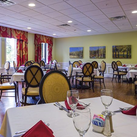 An elegant dining room with neatly arranged tables and chairs, featuring vibrant artwork and ample natural light.