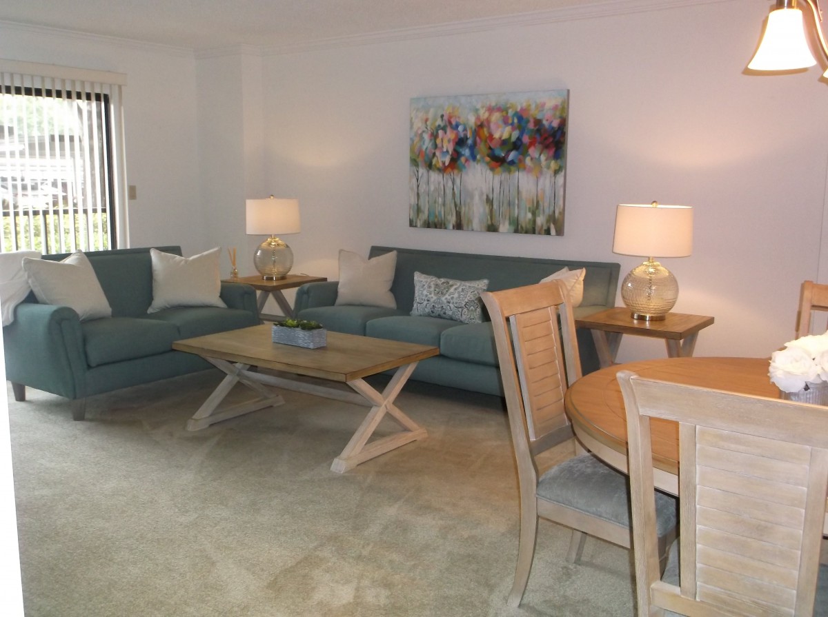A cozy living room featuring two sofas, a coffee table, dining set, and decorative lamps with artwork on the wall.