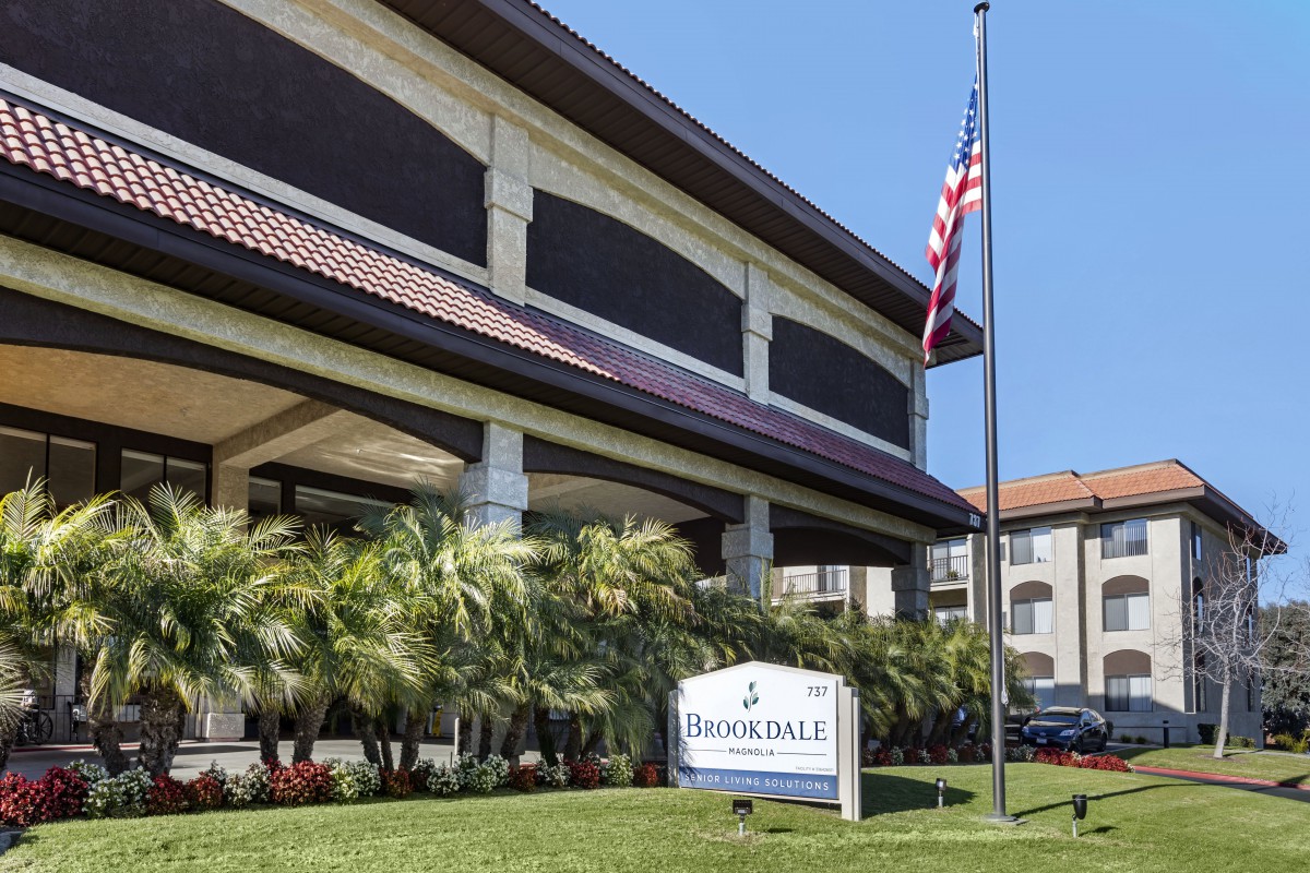 A building entrance with a sign and an American flag in front, surrounded by palm trees.