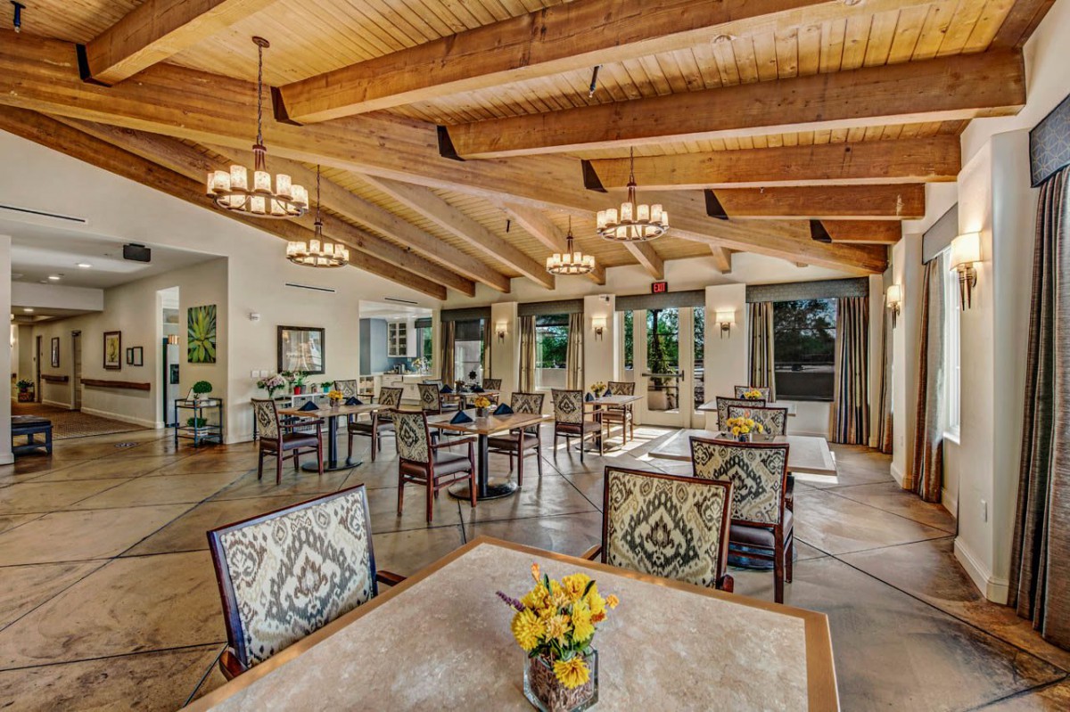 A spacious dining room with wooden beams, elegant chandeliers, and beautifully decorated tables.
