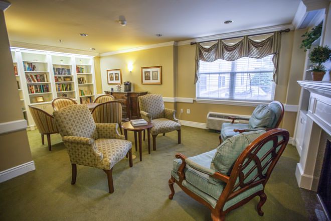 A cozy living room with several chairs, a small table, and bookshelves in the corner.