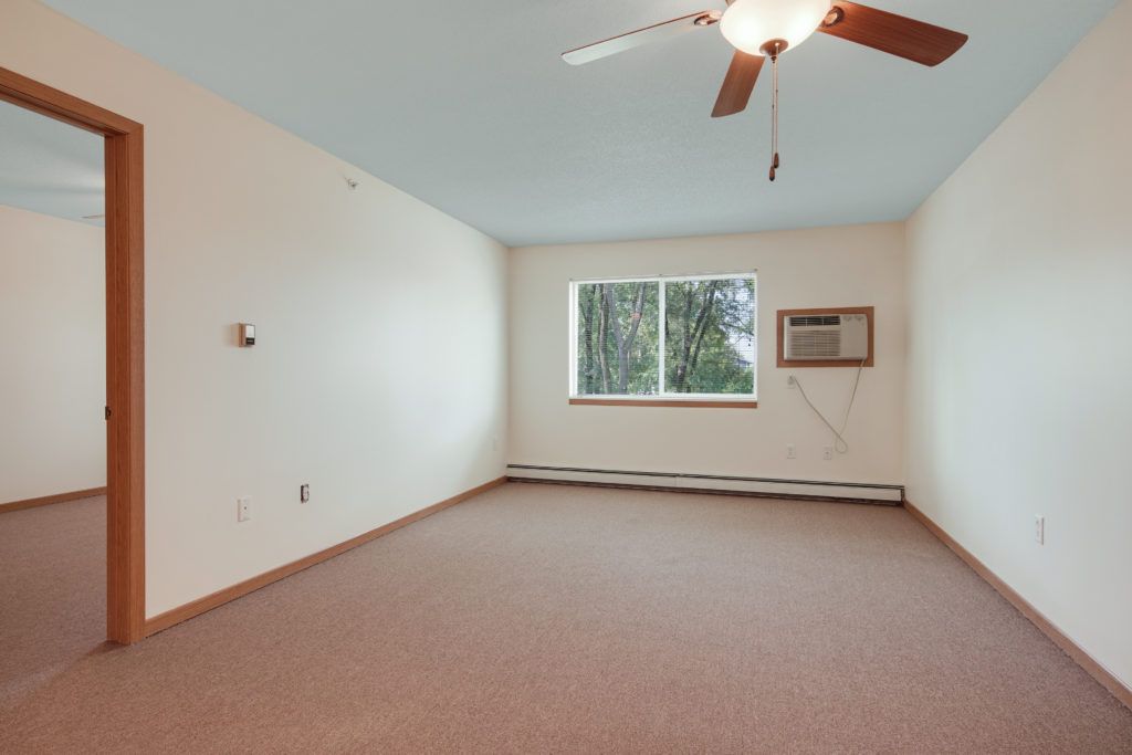 An empty room with a ceiling fan, carpeted flooring, and an air conditioner installed in the window.