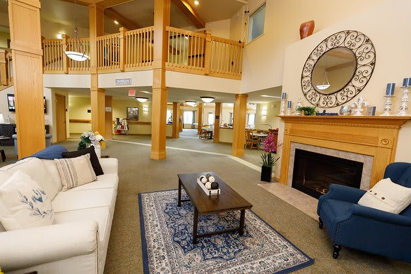 A spacious and warmly decorated living room with a cozy fireplace, comfortable seating, and a wooden balcony overhead.