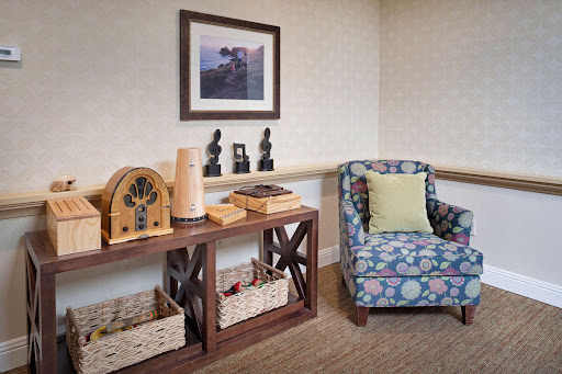 A cozy corner featuring a floral-patterned chair and a wooden shelf with decorative items and storage baskets.