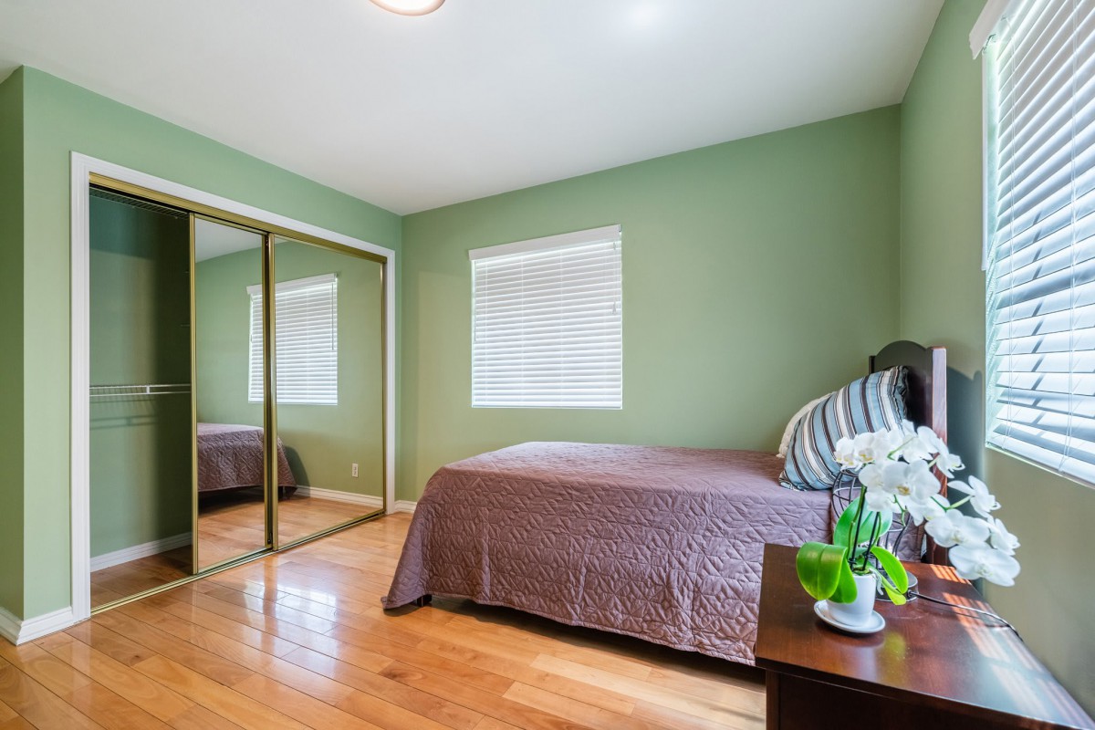 A cozy bedroom with green walls, hardwood flooring, a bed with brown bedding, and a mirrored closet.