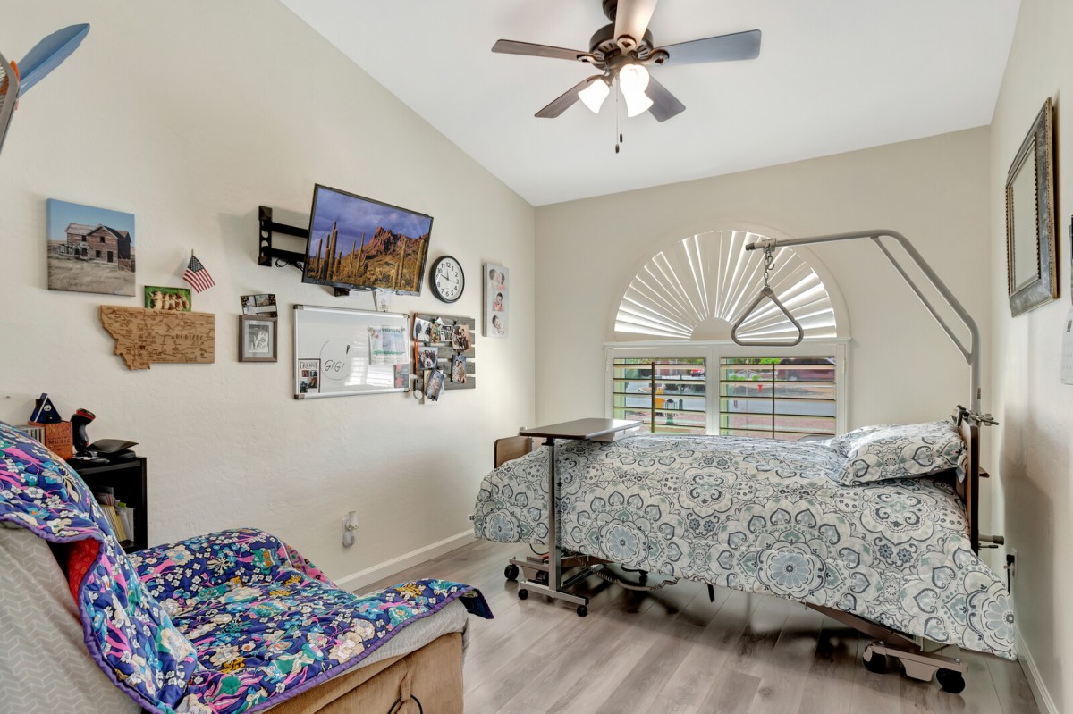 A cozy bedroom featuring a hospital bed, wall-mounted TV, and an armchair by the window with elegant decor.