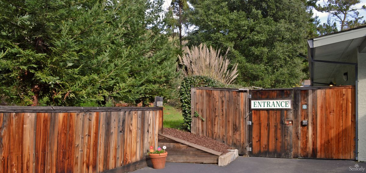 A wooden gate marks the entrance to a garden surrounded by lush greenery.