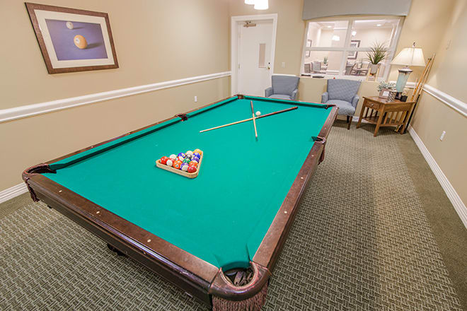 A pool table setup in an indoor game room with a cue stick and racked balls.