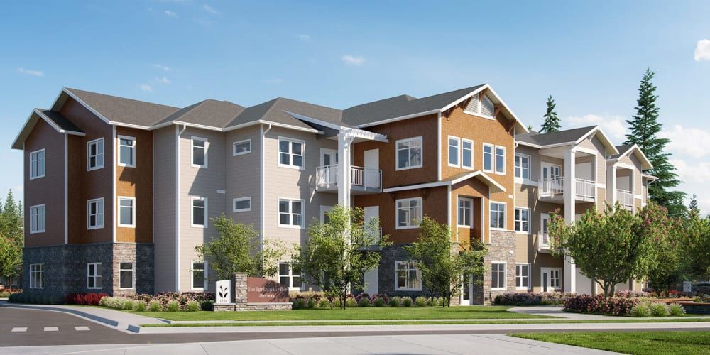 A modern apartment building with a mix of beige and brown siding, surrounded by trees and greenery.
