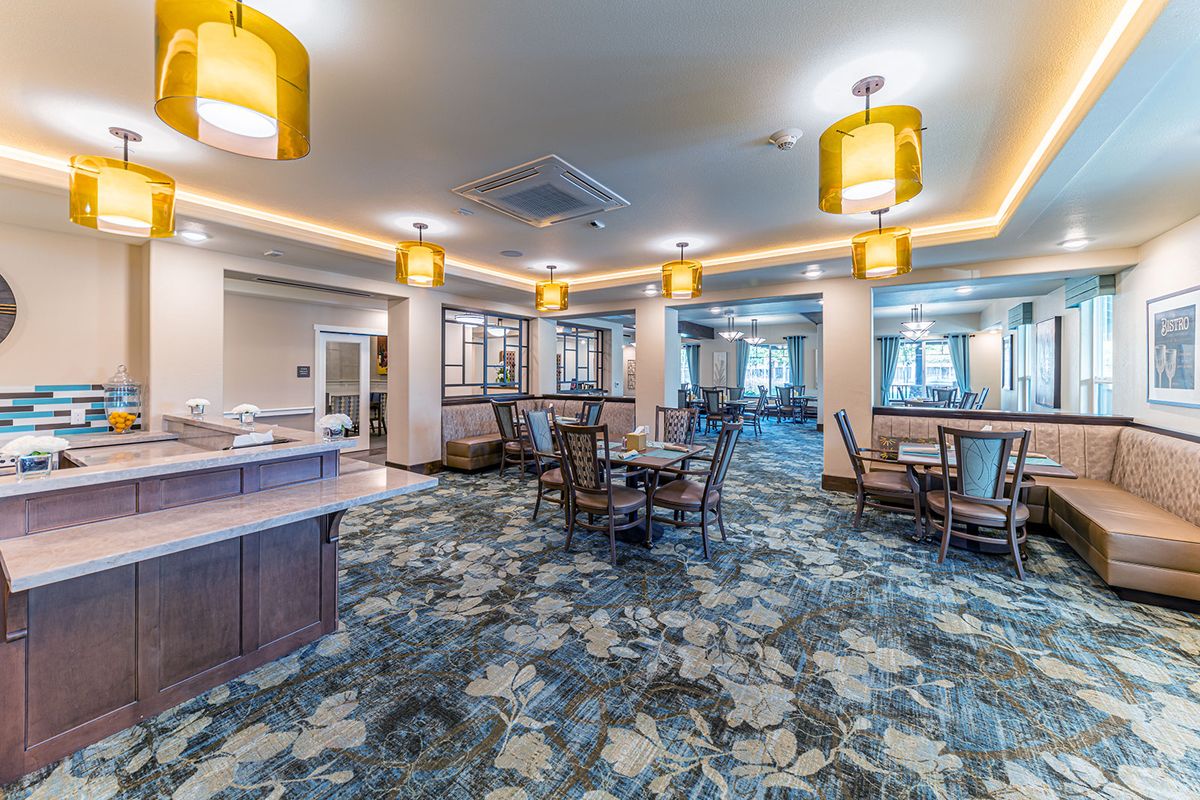 A well-lit lounge area with dining tables and chairs, featuring ornate lighting fixtures and a patterned carpet.