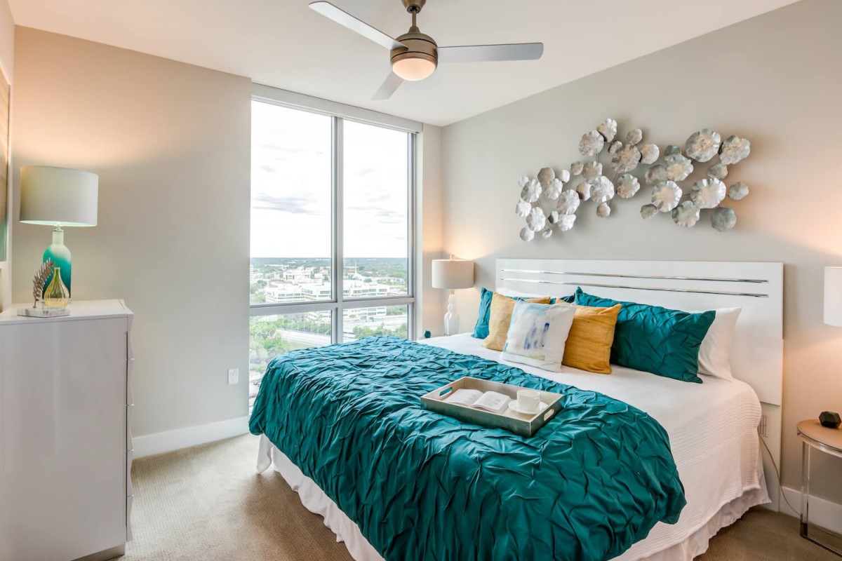 Modern bedroom with teal bedding and natural light from large windows.
