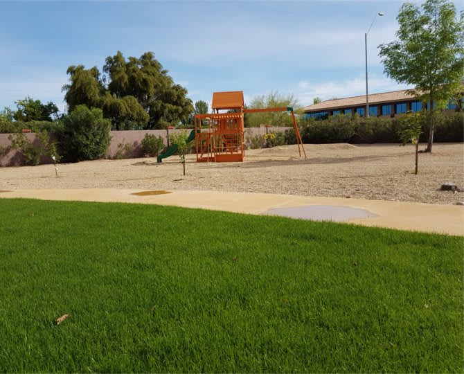 A sunny outdoor playground surrounded by grass and trees.