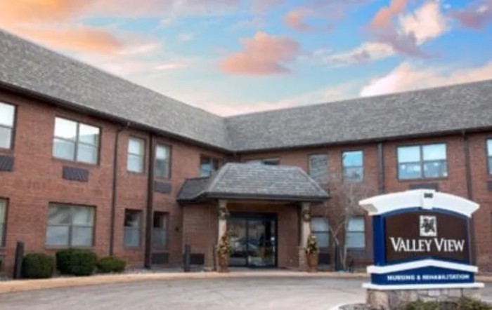 A brick building with a welcoming entrance and a sign outside, set against a colorful sky.