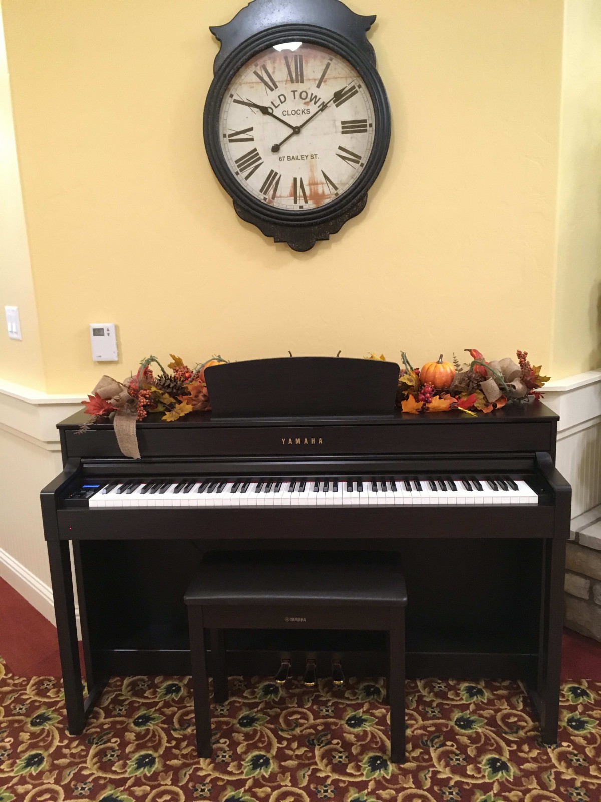 A digital piano adorned with autumn leaves sits beneath a wall clock.