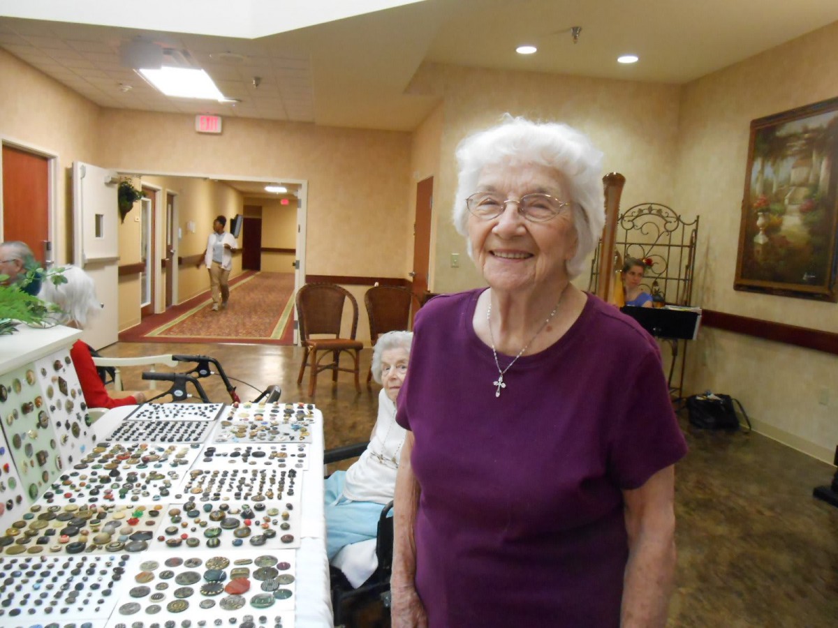 An elderly woman smiling next to a display table with artifacts.