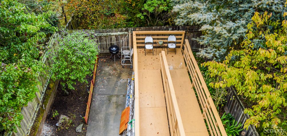 A wooden deck with seating and a grill, surrounded by lush greenery.