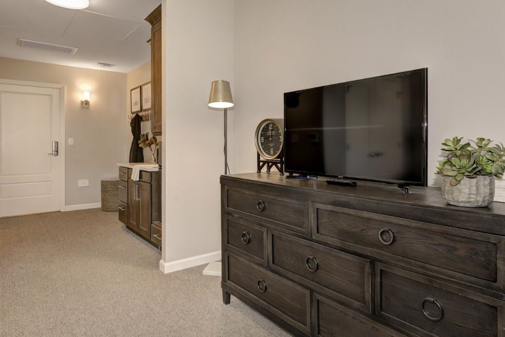A cozy bedroom setup featuring a dresser with a television and a floor lamp.
